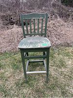 Front view of the wooden green painted chair showing paint chips and worn seat.