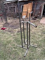 Full view of metal clothing rack standing on grass outdoors, showing three arms and vertical frame.