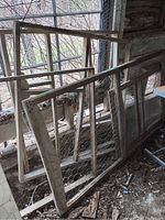 Set of old wooden frames with chicken wire and window frame leaning against wooden structure in barn space.
