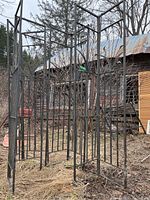 Four black metal decorative garden gate corners with curved ornamental bars, displayed outdoors against a barn and field background.