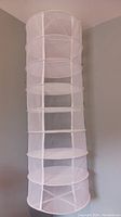 Full view of the white mesh herb dryer, showing the cylindrical shape with multiple drying shelves.