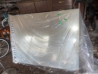 Full view of large vintage mirror wrapped in clear plastic in a barn, showing label and overall size.