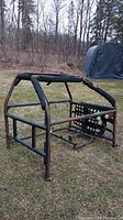 Roll cage placed on grass showing rectangular metal frame with padding and rust.