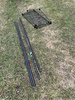 Photo of black metal rods and wire mesh shelf for shelving unit laid out on grass, showing unassembled shelving components.
