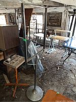 Standing metal sign frame with round base, rusty condition, rectangular 29x22 inch frame, 67 inches tall stand visible in a barn with other furniture.