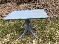 Front angled view of the gray chalk paint table with scalloped edges and folding top side panel, standing on grass outdoors.