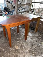 Square wooden table and side table seen in barn environment with dirt floor, showing wood finish and surface wear.