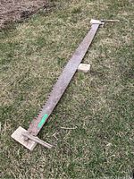 Image showing full length of rusty two-man saw laid on grass with wooden handles at each end.