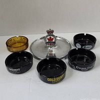 Overview of all six ashtrays showing five glass promotional casino ashtrays and one metal Legion ashtray.