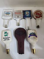 Photos of 7 assorted beer tap handles arranged on a white background showing brand logos and condition needing cleaning.