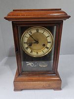 Front view of wooden mantel clock with glass front showcasing the clock face with Roman numerals and winding key inside the base.