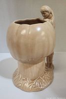 Front left angle of light beige ceramic cookie jar shaped as a pumpkin with boy figure attached.