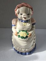 Front view of the ceramic cookie jar shaped as a pig holding a flower basket wearing an apron and bonnet.
