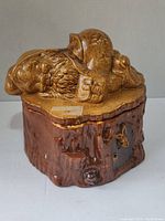 Front-left side view of ceramic cookie jar shaped like a brown tree stump with a sleeping Santa Claus figure lid
