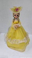 Full view of the vintage Korean doll in yellow dress and hat from front, showing layering and lace details.