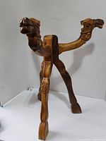 Foldable wooden table base carved in animal shape resembling a camel, showing detailed carving and foldable legs.