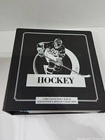 Front cover of black hockey card collector's album binder with hockey player graphic and labels.