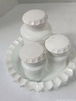 Set of three white glass jars with ridged lids on a white scalloped edge dish.
