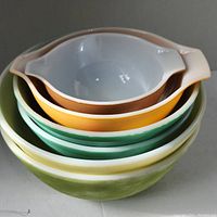 Side view showing stack of six ceramic bowls in green, yellow, orange, and pink colors with pouring spouts and handles on some bowls, slight chipping on edges visible.