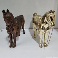Front view of two horse figurines, brass and copper colors, standing side by side on a white surface
