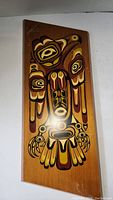 Vertical wooden panel with stylized indigenous figure painted in earth tones.