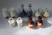 Five pairs of assorted salt and pepper shakers arranged in two rows on a white surface.