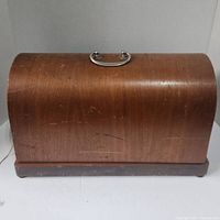 Front view of curved wooden carrying case with silver handle on top, surface worn with scratches