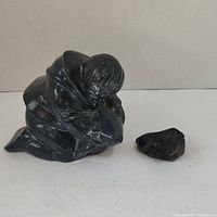 Front angle of two black stone figurines on white surface, one of a child holding a bear, one smaller bear cub separate