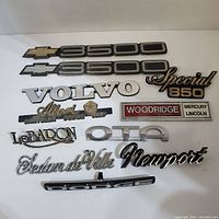 Photo showing various vehicle emblems including Chevrolet 3500, Volvo, Special 850, dealership badges, and model nameplates.