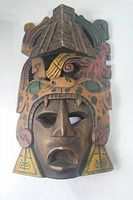 Front view of the wooden mask showing detailed carving, painted headdress, earrings, and facial features.