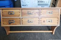 Front view showing the six drawers with metal label holders and wood grain.