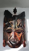 Front view of the carved wooden Kenyan mask showing detailed painted geometric patterns and animal motifs.
