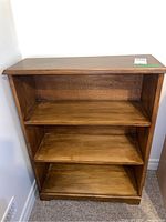 Front view of medium brown wood bookcase with three shelves, showing wear consistent with refinishing and natural grain.