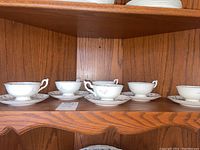 Six white porcelain Coalport tea cups and saucers displayed on a wooden shelf.