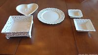 Wide shot showing five white ceramic dishes with lace edge patterns arranged on table