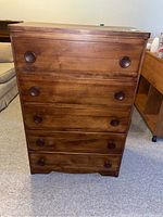 Front view of mid-century wooden dresser showing five drawers with circular recessed wooden pulls and smooth wood finish.