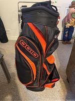 Full side view of the golf bag showing the black and orange color, OGIO logo, and multiple compartments.