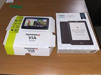 Photo showing TomTom VIA 1505M GPS device box and Kobo E-reader box on a brown table.