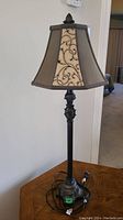 Full view of the table lamp showing metal base with ornate detailing and fabric shade with patterned panels.