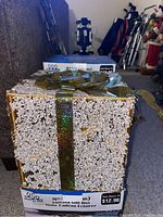 Lighted gift box yard sculpture with white textured body and holographic green-gold ribbon and bow on top, shown with packaging showing brand Holiday Time and size 8 inch (20 cm)