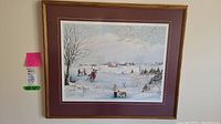 Framed winter scene print by Mary Farkas depicting people skating on a frozen pond with winter landscape and village in the background.