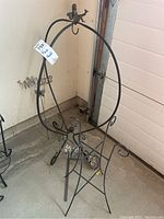 Photo of black metal circular plant stand with curly legs and a small metal butterfly attached near the base.