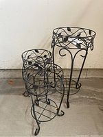 Three metal plant stands with decorative leaf designs, two smaller and one larger, shown from front angle.