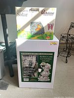 Both boxed solar lights together. Parkline box shows butterfly solar light image; Vectacore box shows 'Rebecca's Guiding Light' statue image with garden angel child figure.