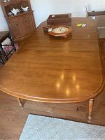 Top view of wood dining table showing extended surface with leaves attached, warm wood tone and smooth finish.