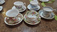 Five assorted teacups and saucers arranged on table showing floral and gold accent designs