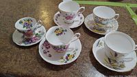 Five teacups with matching saucers arranged on a table, showing variety of floral designs and styles.