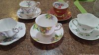 Overview of all five teacups and saucers showing floral, red/gold, and green shamrock patterns.
