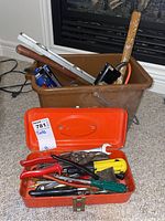 Brown plastic bucket containing wooden-handled hammer, metal pipe wrench, spirit level and longer handled tools.