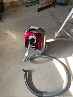 Full view of Shark canister vacuum cleaner on garage floor with hose and curved attachment.